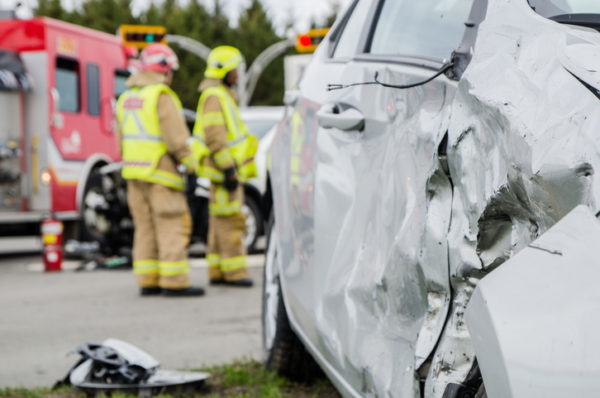 Close up on a car crashed during an accident with two firemen in background with firetruck 