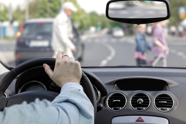 View from inside a car as a driver yields to pedestrians crossing the street at a crosswalk.