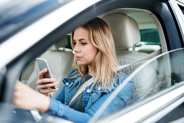 A driver in a business suit holding a smartphone while behind the wheel, illustrating a common cause of serious distracted driving crashes in the Dallas-Fort Worth area.